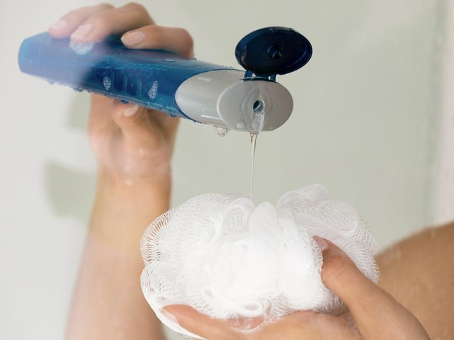 Close up young woman pouring liquid moisturizing soap shower gel from cosmetic bottle on loofah puff, enjoying morning evening body cleansing routine, removing dead cells exfoliating in bathroom.