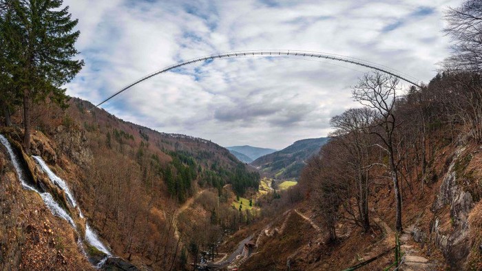 Jerman Bangun Jembatan Gantung untuk Wisata di Hutan Hitam TOPSHOT - A panorama of 27 pictures taken on March 3, 2023 shows a suspended footbridge under construction, overlooking a waterfall in Todtnau, southwestern Germany. - The construction of the 450 meters long bridge suspended at a height of up to 120 meters is expected to be completed in May 2023 and to become a major tourist attraction in the Black Forest. (Photo by PATRICK HERTZOG / AFP) (Photo by PATRICK HERTZOG/AFP via Getty Images)