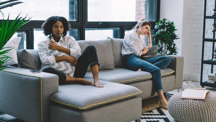 Portrait of offended dark skinned hipster girl sitting on cozy couch with disappointed fellow, unhappy multicultural friends dont talk after quarrel in modern apartment feeling stress from problems