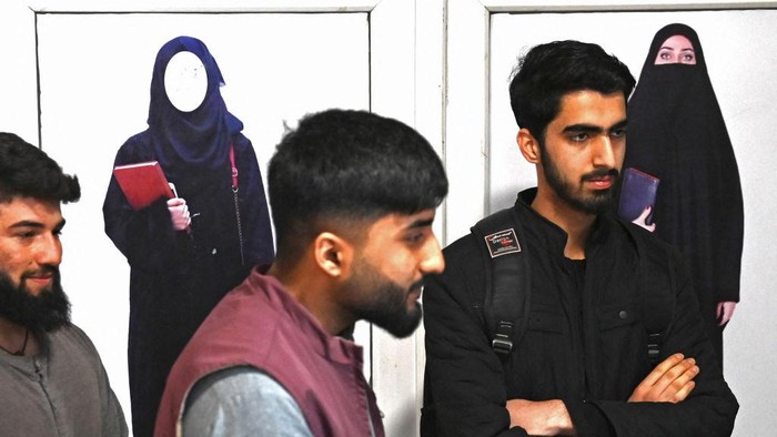 Kampus di Afghanistan Dibuka Kembali, tapi Perempuan Dilarang Masuk TOPSHOT - Male students stand in front of a poster ordering women to cover themselves with a Hijab, in the corridor of a private university after the universities were reopened in Kabul on March 6, 2023. - Male students trickled back to their classes on March 6 after Afghan universities reopened following a winter break but women remain barred by Taliban authorities. (Photo by Wakil KOHSAR / AFP) (Photo by WAKIL KOHSAR/AFP via Getty Images)