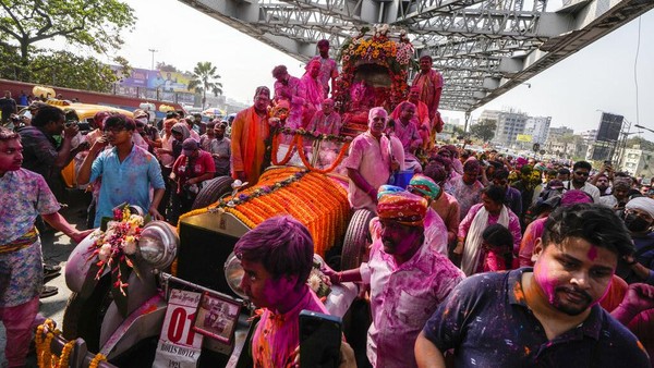 Umat Hindu berkerumun di sekitar mobil Rolls Royce 1921 yang dimodifikasi membawa patung dewa Krishna melalui bangunan bersejarah Howrah Bridge selama festival Holi di Kolkata, India, Minggu (5/3/2023). AP/Bikas Das  