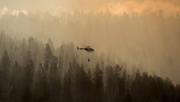 Sebuah helikopter dari pemadam kebakaran membawa air untuk dijatuhkan di atas api yang membakar hutan.  