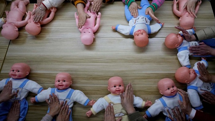 Women holding plastic baby dolls, wait to enter a classroom before a nursing skills class for confinement carers, at Yipeitong training centre in Shanghai, China March 2, 2023. REUTERS/Aly Song
