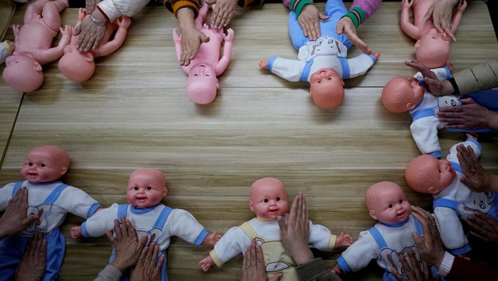 Melihat Pelatihan Merawat Bayi di Shanghai Women holding plastic baby dolls, wait to enter a classroom before a nursing skills class for confinement carers, at Yipeitong training centre in Shanghai, China March 2, 2023. REUTERS/Aly Song