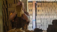 Seorang pekerja wanita tengah mencetak tanah liat mejadi batu bata.