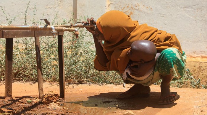 Miris, Pengungsi Somalia Kelaparan hingga Dehidrasi Imbas Kekeringan An internally displaced Somali woman holds her child as she drinks water from a tap outside the feeding centre, a new site for IDPs, in Barwaaqo, near Baidoa, Somalia, February 21, 2023. REUTERS/Feisal Omar