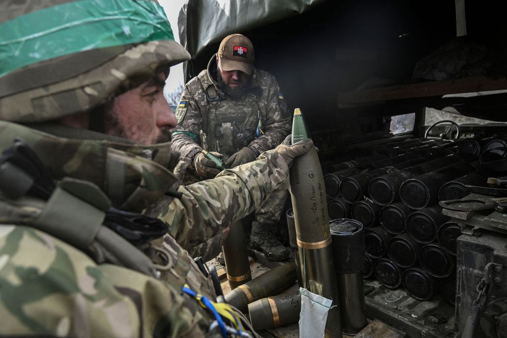 Seorang tentara Ukraina berlindung saat dia memegang cangkang howitzer 105mm di dekat kota Bakhmut, pada 8 Maret 2023, di tengah invasi Rusia ke Ukraina. (AFP via Getty Images/ARIS MESSINIS)