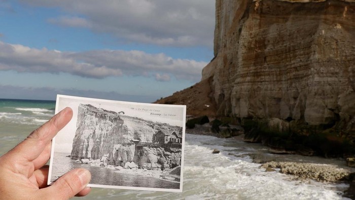 A person holds a photo of the Cap Fagnet cliff, taken decades before part of it crashed into the sea in February due to coastal erosion, in front of the damaged cliff in Fecamp, France, March 03, 2023. REUTERS/Pascal Rossignol