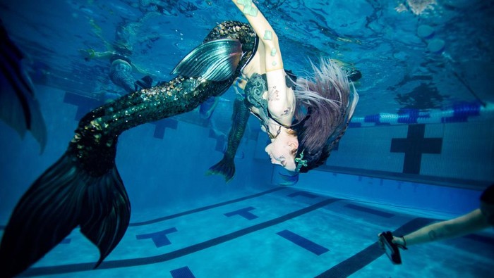 Serunya Ratusan Putri Duyung Nongkrong Bareng di AS People dressed as mermaids and mermen sit on the side of the pool as they await the group photo and group swim during the MerMagic Convention at the Freedom Aquatic & Fitness Center in Manassas, Virginia on March 4, 2023. - The event bills itself as the