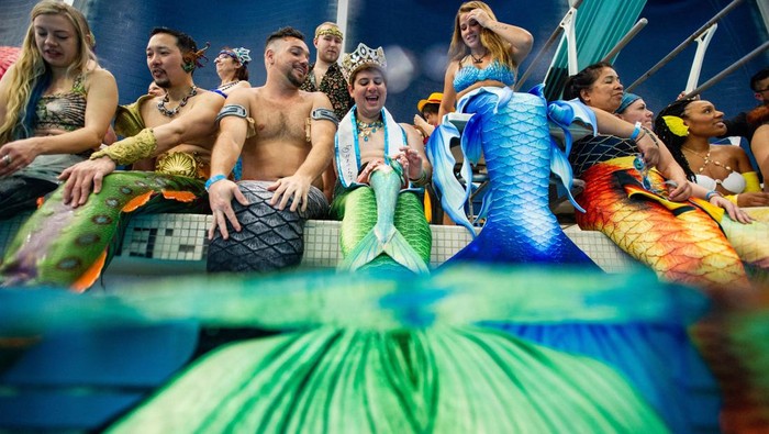 People dressed as mermaids and mermen sit on the side of the pool as they await the group photo and group swim during the MerMagic Convention at the Freedom Aquatic & Fitness Center in Manassas, Virginia on March 4, 2023. - The event bills itself as the 