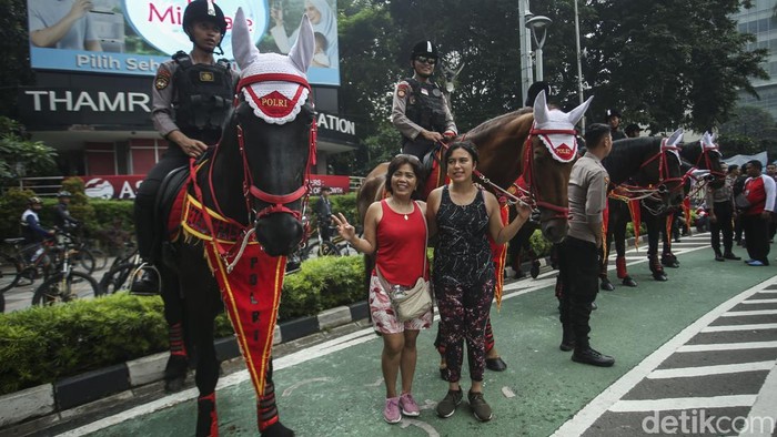Saat Polisi Berkuda Jadi Primadona di CFD Jakarta Polisi menggendong seorang anak untuk menaikkannya ke atas kuda di Bundaran HI, Jakarta, Minggu (12/3/2023).