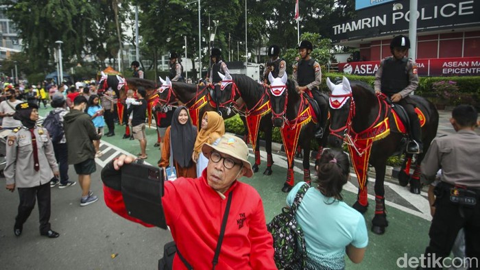 Saat Polisi Berkuda Jadi Primadona di CFD Jakarta Polisi menggendong seorang anak untuk menaikkannya ke atas kuda di Bundaran HI, Jakarta, Minggu (12/3/2023).