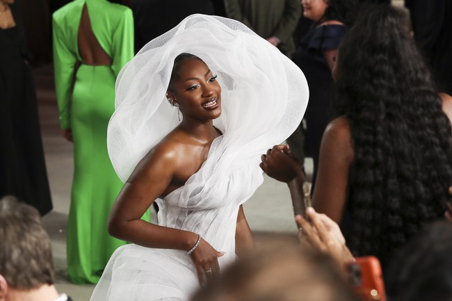 Penyanyi Tems hadir dengan gaun putih bergaya avant-garde yang dilengkapi hiasan dramatis pada bagian punggung. Netizen sempat membicarakan gaun Tems yang menghalangi penonton di belakangnya. Pilihan yang kurang bijak. (Foto: Getty Images)