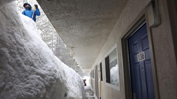 Warga menyekop gundukan salju di sebuah motel saat salju terus turun di pegunungan Sierra Nevada, di Danau Mammoth, California, Sabtu (11/3/2023).  