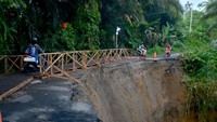 Warga mengendarai sepeda motor melewati jembatan darurat yang baru dibangun akibat jalan longsor, di Nagari Gunung Padang Alai, Kabupaten Padang Pariaman, Sumatera Barat.