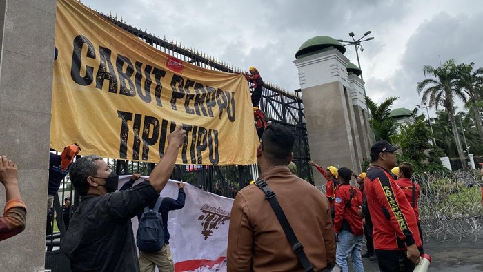Massa buruh geser kawat berduri depan gerbang DPR RI dan memanjat untuk pasang spanduk besar.