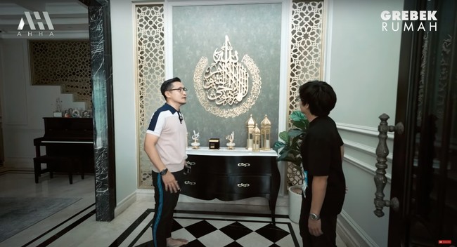 Masuk ke dalam rumah disambut dengan pajangan dinding berupa ayat kursi. Pada bagian bawahnya terdapat meja kecil yang dihiasi dengan pajangan-pajangan, seperti miniatur kabah. Foto: YouTube/AH
