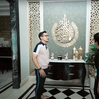 Masuk ke dalam rumah disambut dengan pajangan dinding berupa ayat kursi. Pada bagian bawahnya terdapat meja kecil yang dihiasi dengan pajangan-pajangan, seperti miniatur kabah. Foto: YouTube/AH