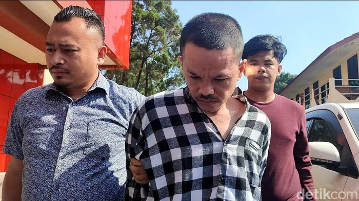 Polisi menangkap pelaku mutilasi mayat dalam koper merah yang ditemukan di Tenjo, Bogor. Pelaku memakai kemeja kotak-kotak berwarna hitam dan putih.