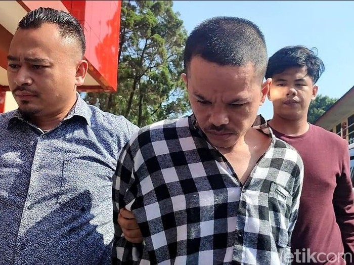 Polisi menangkap pelaku mutilasi mayat dalam koper merah yang ditemukan di Tenjo, Bogor. Pelaku memakai kemeja kotak-kotak berwarna hitam dan putih.