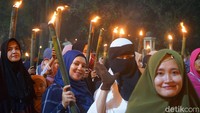 Barisan rombongan pawai obor yang berjalan kaki terlihat berada mengikuti mobil komando. Emak-emak berserta anak-anak terlihat berada di barisan paling depan.