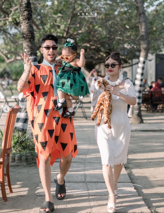 Siti Badriah dengan gaun putih dan kalaung mutiaranya cosplay menjadi karakter Wilma Flinstone, sementara sang suami mengenakan kostum ikonik berwarna oranye lengkap dengan dasi biru milik karakter suami Wilma, Fred Flinstone. Sama-sama mengenakan kaca mata hitam, ketiganya tampak begitu menawan. Foto: Instagram/@krisjianabah