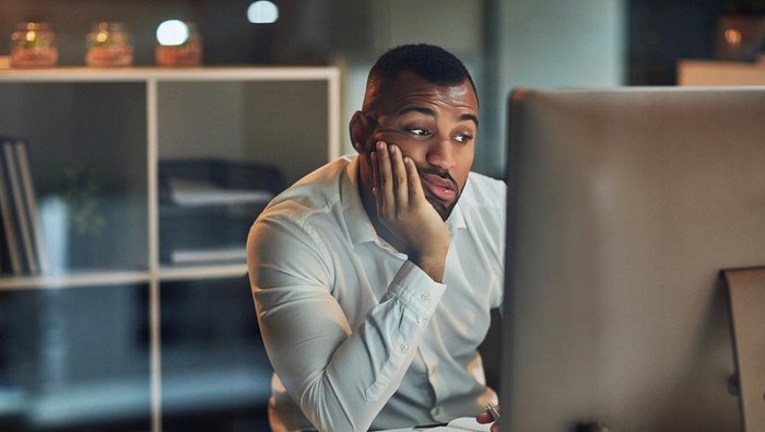 Shot of a young businessman looking bored while working at his desk during late night at work