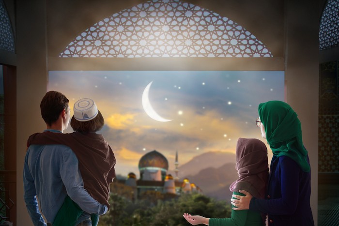 Ramadan Kareem greeting. Family at window looking at Islamic city with mosque skyline, crescent moon and stars. Muslim parents and children pray. Mother, father and kids celebrate end of fasting.