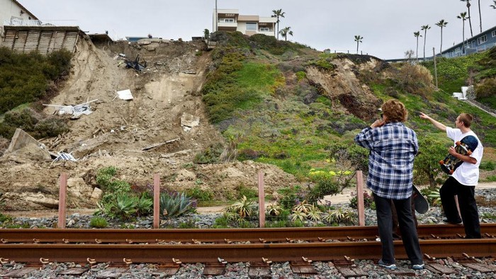 SAN CLEMENTE, CALIFORNIA - MARCH 16: People view a hillside landslide brought on by heavy rains, which caused four ocean view apartment buildings to be evacuated and shuttered due to unstable conditions, on March 16, 2023 in San Clemente, California. Weeks of rains loosened the soil in Orange County which tumbled down near railroad tracks that run next to the beach below. (Photo by Mario Tama/Getty Images)
