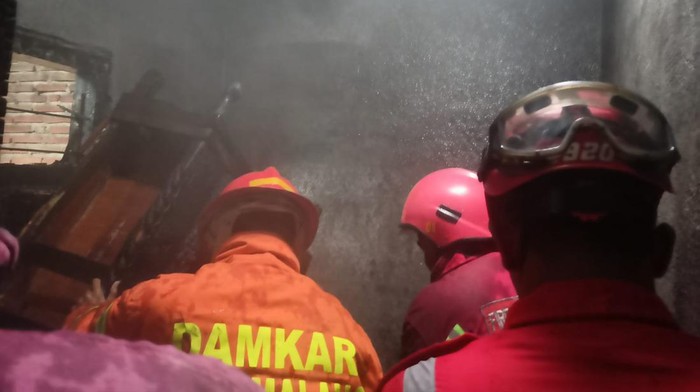 Petugas melakukan pembasahan rumah yang terbakar di Malang