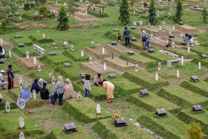 Indonesian Muslims readings from the Quran during make pilgrimages to their familys graves to pray ahead of the holy month of Ramadan at a cemetery for COVID-19 victims on March 19, 2023 in Medan, Indonesia.  Muslims from Indonesia are getting ready to welcome the holy month of Ramadan by cleaning themselves bathing in the river and cleaning family graves. Colorful street parades take place along with family rituals and a large-scale party ending with Eid al-Fitr celebrations. (Photo by Ivan Damanik/NurPhoto via Getty Images)