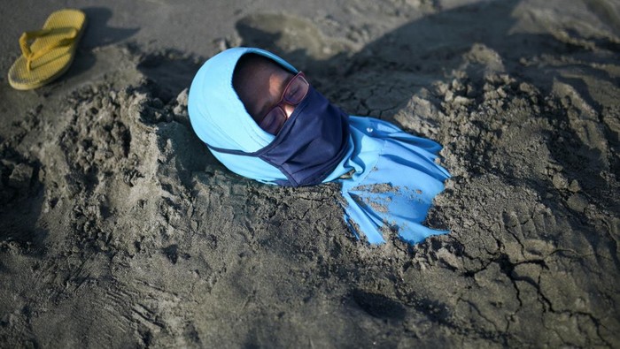 Nurmalawati lies covered with black sand during a traditional therapy, that is believed to have therapeutic properties, at Syiah Kuala beach in Aceh, Indonesia March 19, 2023. REUTERS/Riska Munawarah