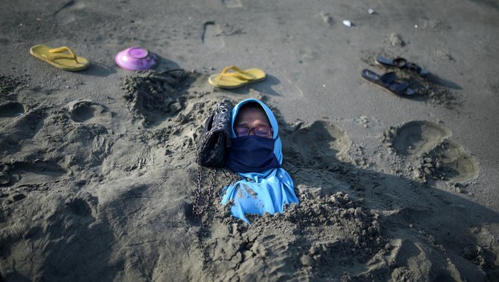 Nurmalawati lies covered with black sand during a traditional therapy, that is believed to have therapeutic properties, at Syiah Kuala beach in Aceh, Indonesia March 19, 2023. REUTERS/Riska Munawarah