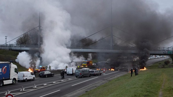 Prancis Memanas, Jalan Raya di Rennes Diblokir Police officers work near a burning barricade on a highway amid a protest against pension reform, in Rennes, France, March 20, 2023, in this image obtained from social media. Twitter @DHR_Damien/via REUTERS THIS IMAGE HAS BEEN SUPPLIED BY A THIRD PARTY. NO RESALES. NO ARCHIVES. MANDATORY CREDIT