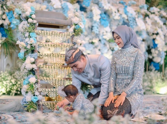 Dalam unggahan yang dibagikan terlihat acara tedak sinten baby Moana digelar dengan mewah didominasi warna biru. Dekorasinya tampak dipenuhi bunga-bunga yang juga berwarna biru, senada dengan pakaian yang dikenakan Ricis, Ryan, dan baby Moana. Foto: Instagram/@windrafotografi