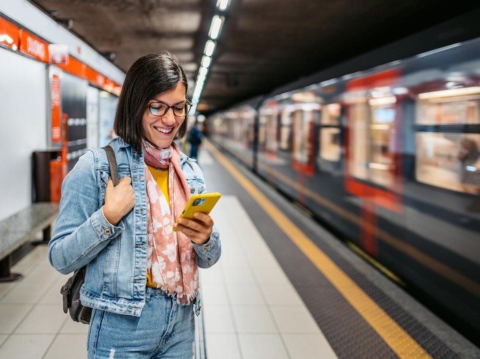 Beautiful young woman using smart phone in a subway station while waiting for her subway.