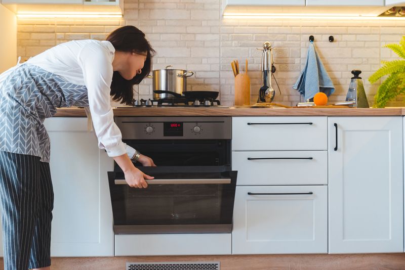 young pretty woman open oven to cook. domestic kitchen concept. copy space