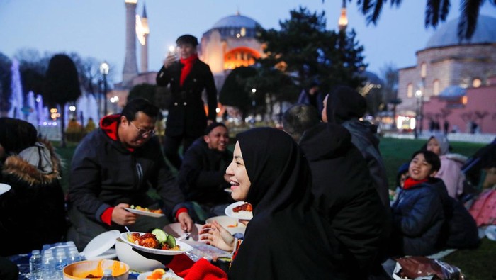 People, with the Ayasofya-i Kebir Camii or Hagia Sophia Grand Mosque in the background, have their iftar (breaking fast) meal at Sultanahmet Square during first day of the holy month of Ramadan in Istanbul, Turkey, March 23, 2023. REUTERS/Dilara Senkaya
