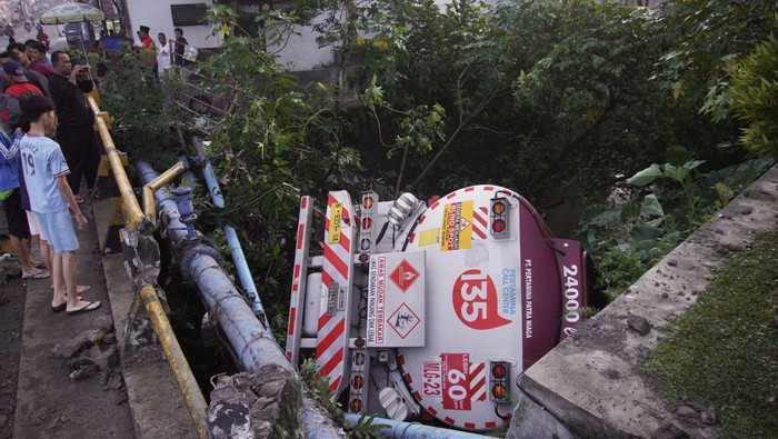 Warga mengamati kondisi truk tangki BBM ber nopol N 9359 UA yang terperosok ke sungai di Desa Bululawang, Malang, Jawa Timur, Minggu (26/3/2023). Kecelakaan tunggal truk tangki yang terjadi sekitar pukul 01.50 WIB tersebut diduga akibat manuver sopir untuk menghindari kendaraan yang tiba-tiba muncul dan menyebabkan satu orang mengalami luka-luka. ANTARA FOTO/Irfan Sumanjaya/Zk/hp.