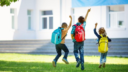 Children with rucksacks jumping in the park near school. Pupils with books and backpacks outdoors