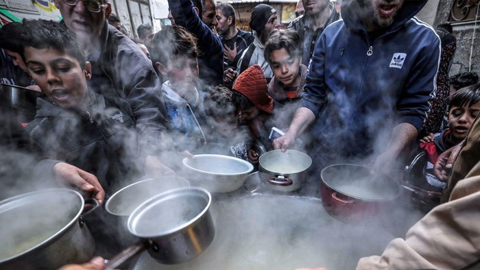 TOPSHOT - Palestinian Walid al-Hattab (top R) hands out soup from a large pot to impoverished youths to break their fast on the second day of the Muslim holy month of Ramadan in Gaza City on March 24, 2023. (Photo by MOHAMMED ABED / AFP) (Photo by MOHAMMED ABED/AFP via Getty Images)