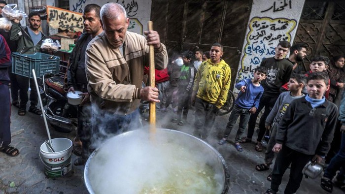 Potret Berbagi Sup Gratis untuk Warga Gaza TOPSHOT - Palestinian Walid al-Hattab (top R) hands out soup from a large pot to impoverished youths to break their fast on the second day of the Muslim holy month of Ramadan in Gaza City on March 24, 2023. (Photo by MOHAMMED ABED / AFP) (Photo by MOHAMMED ABED/AFP via Getty Images)