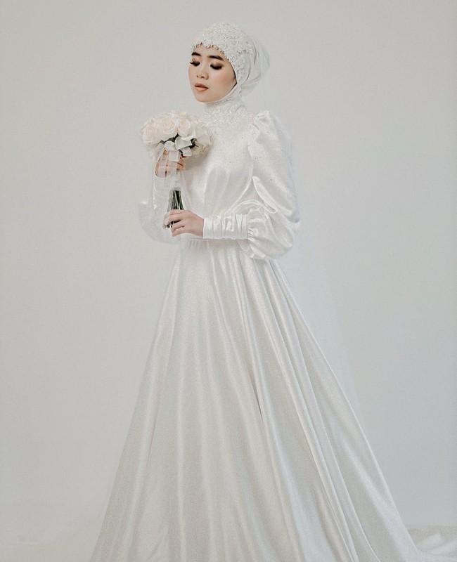 Gaun satin dengan lengan puff cocok untuk pengantin hijab yang ingin mengenakan busana simpel tapi tetap menonjolkan keindahan. Aksen lace pada jilbab dan leher menambah kesan feminin. Foto: Weddingku/ Ivory Bridal