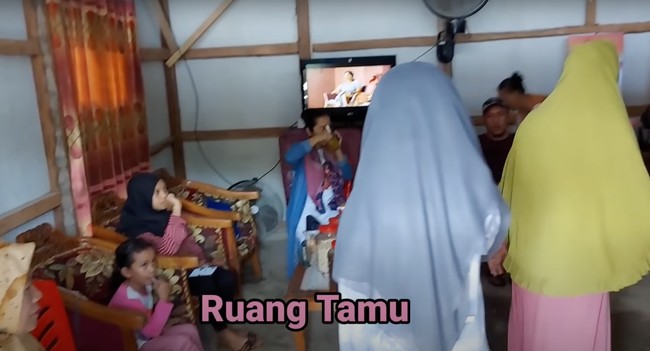 Masuk ke dalam rumah langsung disambut dengan ruang tamu yang juga terlihat sederhana. Ruang tamu tersebut tampak dilengkapi dengan beberapa sofa dan sebuah meja kayu serta televisi. Foto: YouTube/Daily Indah