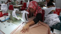 Pekerja menjahit mukena dengan motif yang telah ditentukan.