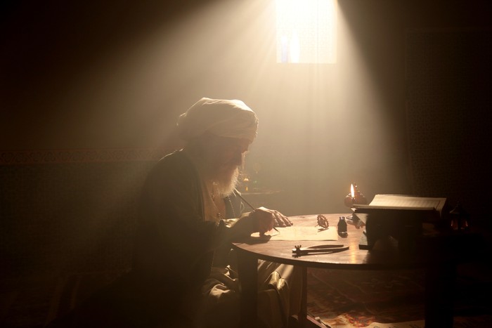 An old and historic Islamic scientist is working in his studio writing, reading and exploring.