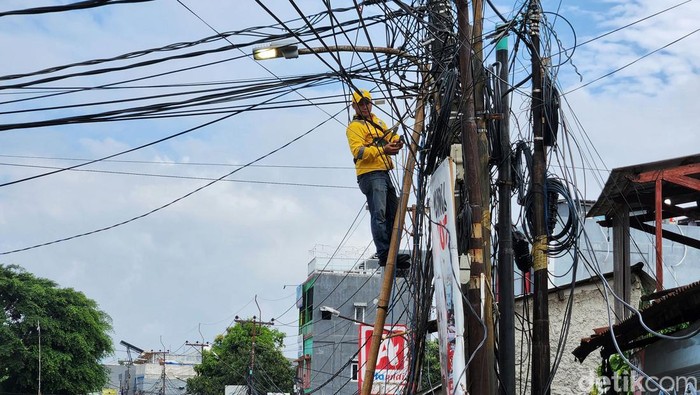 Petugas memperbaiki kabel semrawut di kawasan Pesanggrahan, Jakarta Selatan, Kamis (30/3/2023). Pemprov DKI secara bertahap merelokasi kabel yang semrawut dengan menanam di bawah tanah. Selain estetika, jaringan kabel bawah tanah dinilai lebih aman.