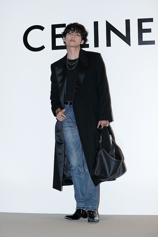 V BTS tampil dengan coat hitam yang dipadukan dengan denim jeans dan koleksi boots CELINE. Foto: Getty Images