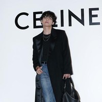 V BTS tampil dengan coat hitam yang dipadukan dengan denim jeans dan koleksi boots CELINE. Foto: Getty Images