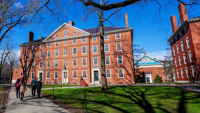 Cambridge, Massachusetts, USA - April 10, 2022: Students walking in Harvard Yard towards freshman dormitory building Hollis Hall . Built in 1763, it is one of the oldest buildings at Harvard College.